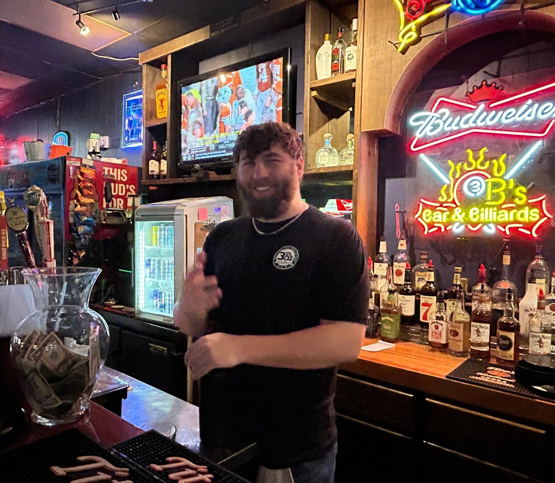 A smiling bartender behind the neon-lit bar