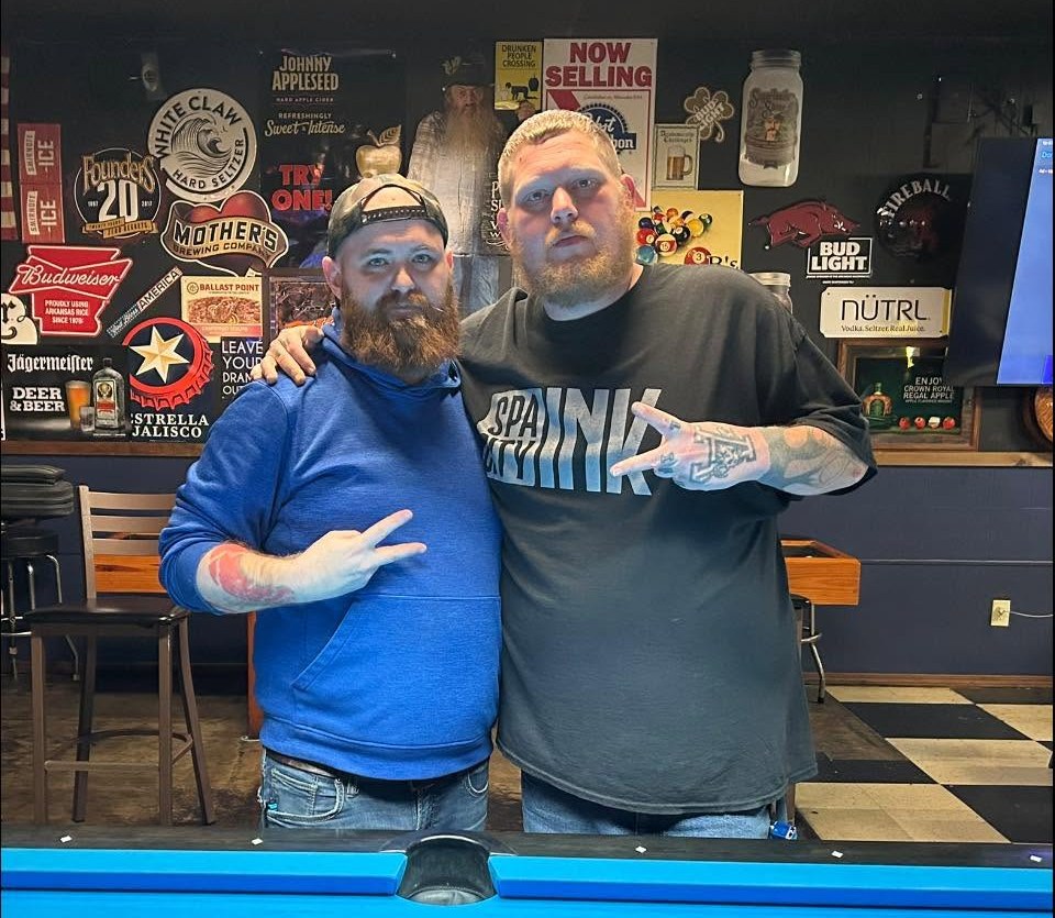 Two men standing together behind a blue pool table at 3B’s
