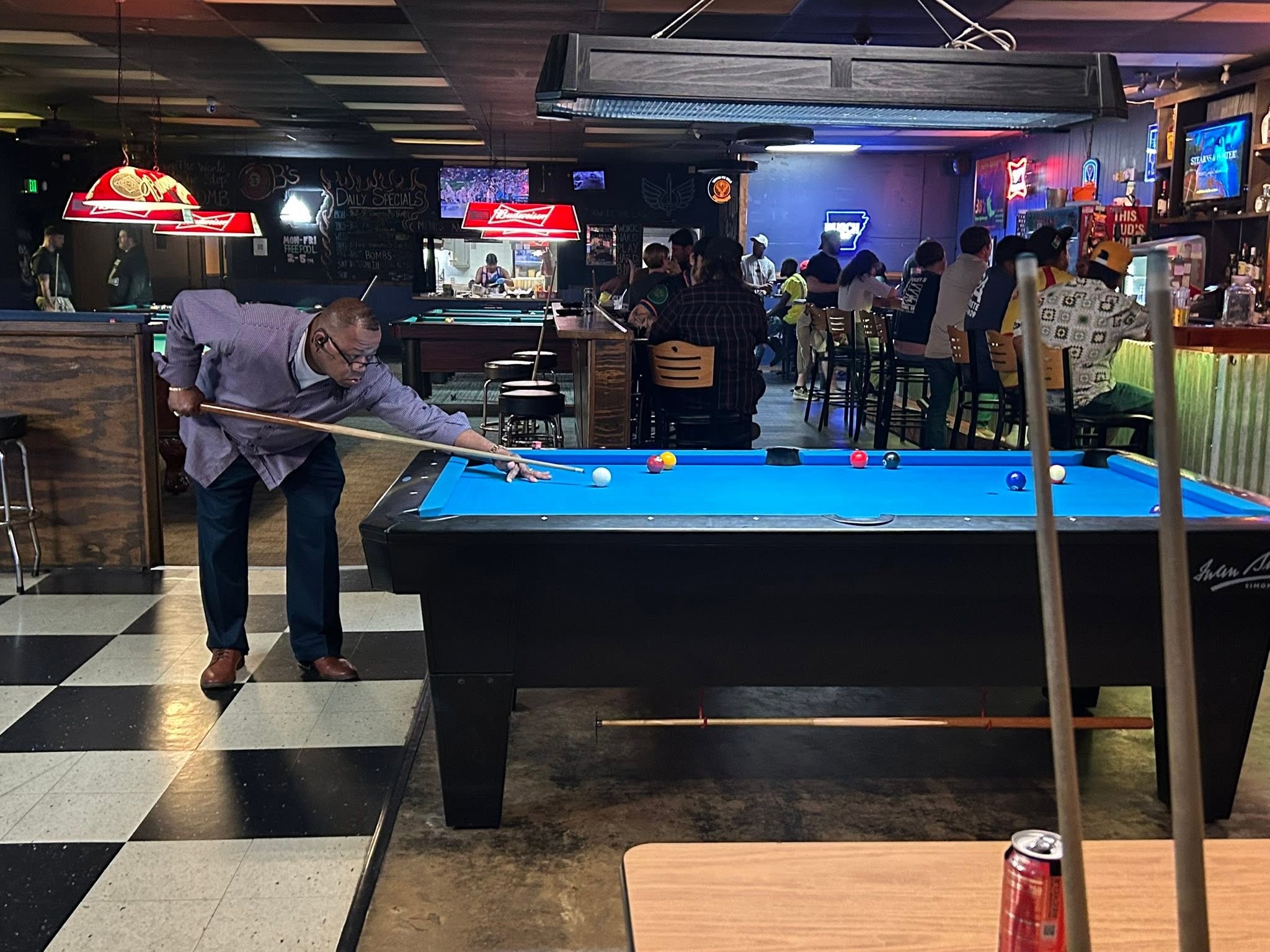 A player lining up a shot across blue felt at 3B’s